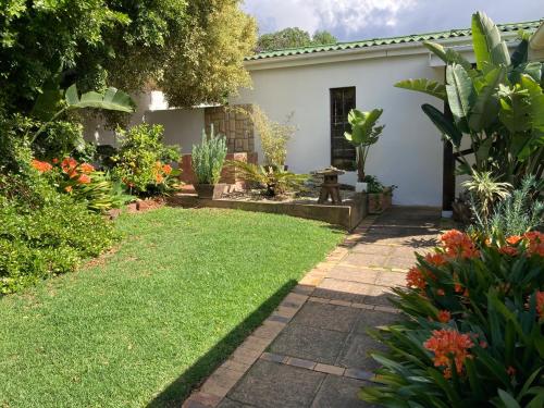 a garden with a white house with a lawn at Haus Barbara Guest House in Bredasdorp