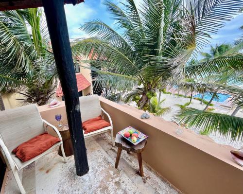 a balcony with two chairs and a table and palm trees at Beachfront Hammock Heaven in Akumal