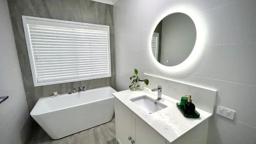 ein Badezimmer mit einem Waschbecken, einer Badewanne und einem Spiegel in der Unterkunft Perfect North Brisbane Retreat 4 bed in Griffin