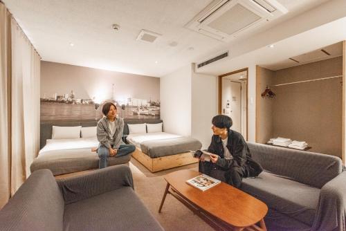 dwie osoby siedzą w pokoju hotelowym w obiekcie Hotel Relief Kokura Annex w mieście Kitakyushu