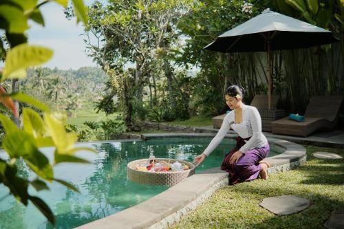 a woman sitting next to a pool with a basket of fruit at Anandari Ubud Villa in Ubud