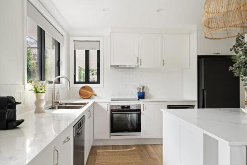 a white kitchen with white cabinets and a black refrigerator at Surf Lodge Avoca Beach Waterfront to Avoca Lake in Avoca Beach