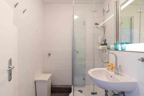 La salle de bains blanche est pourvue d'un lavabo et d'une douche. dans l'établissement Ferienwohnung Pier 1167, à Schilksee