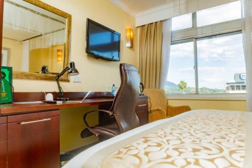 Habitación de hotel con cama, escritorio y espejo. en Sunbird Mount Soche, en Blantyre