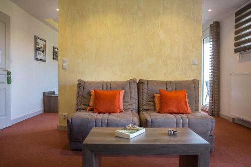 a living room with a couch with orange pillows at Hotel Les Mésanges in Saint-Martin-dʼUriage