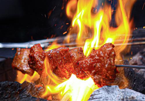 a bunch of meat cooking on a grill with flames at Hudson Resorts in Sriperumbudur
