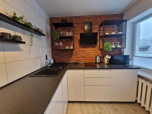 a kitchen with white cabinets and a brick wall at Haustory Apartment in Klaipėda