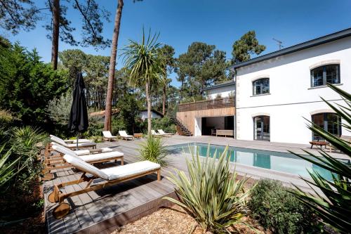 une piscine avec des chaises longues et une maison dans l'établissement Somptueuse Villa sous les pins, à Lège-Cap-Ferret