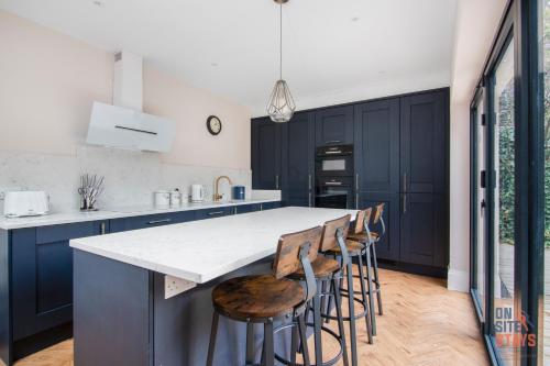 a kitchen with blue cabinets and a counter with stools at OnSiteStays New Large modern 4 bed, Parking, Wifi, 2 x Bathroom in Orpington