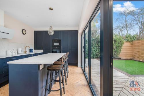 a kitchen with blue cabinets and a counter with bar stools at OnSiteStays New Large modern 4 bed, Parking, Wifi, 2 x Bathroom in Orpington