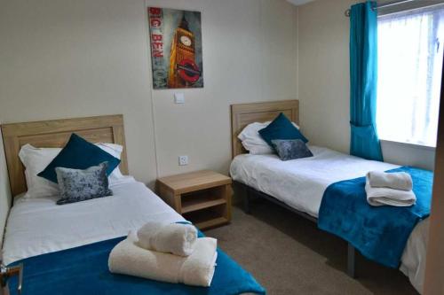 two beds in a room with blue curtains and towels at Bluebell Lodge in Morpeth