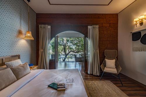 a bedroom with a bed and a chair and a window at SaffronStays Athaang, Dapoli in Ānjarle