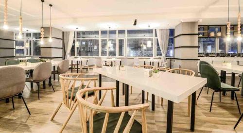 a restaurant with white tables and chairs and windows at Atour Hotel Railway Station Dalian in Dalian