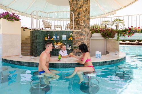 un grupo de personas sentadas alrededor de una mesa en una piscina en Hotel Baia Di Nora en Pula