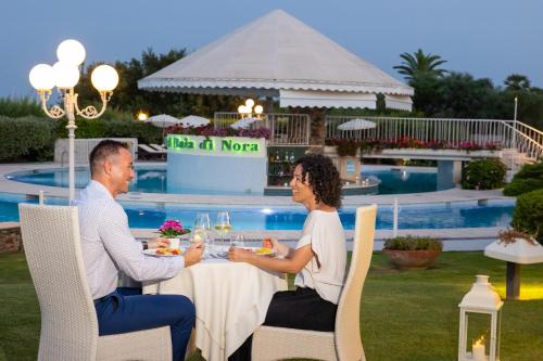 a man and woman sitting at a table near a pool at Hotel Baia Di Nora in Pula