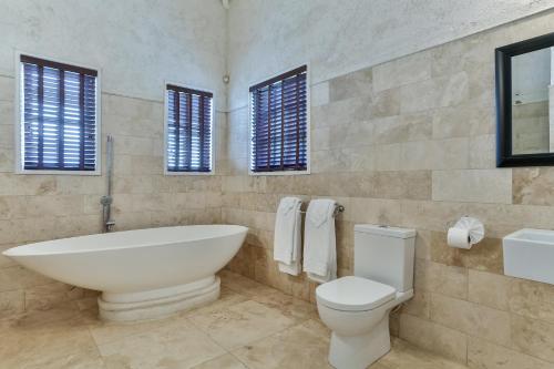 a bathroom with a tub and a toilet and windows at Cayman Villa - Contemporary 4 bedroom Villa with Stunning Ocean Views villa in Cap Estate