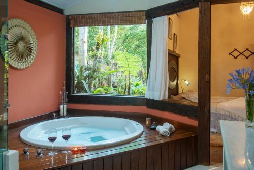 a bathroom with a tub with a window and a bed at Pousada Terra Crua in Visconde De Maua