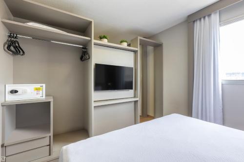 a bedroom with a bed and a flat screen tv at Nobile Suítes Uberlândia in Uberlândia