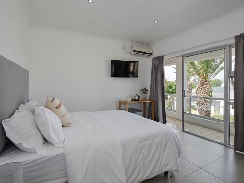 a white bedroom with a bed and a balcony at 19 Beach Road in Cape Town