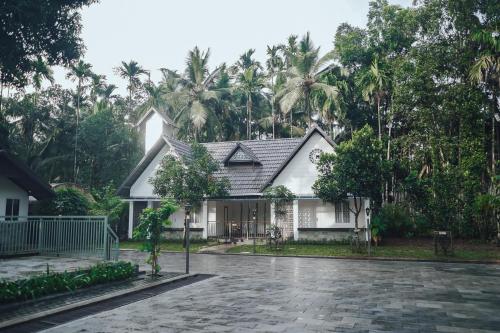 a white house with palm trees in the background at Royad Calicut Farm House - Premium Villa with Pool Inside a Farm in Kozhikode