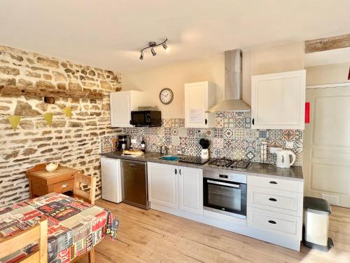 a kitchen with white cabinets and a brick wall at Greener Pastures - Normandy Self Catering Gites in La Chapelle-Engerbold