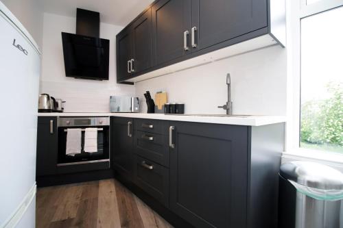 a kitchen with black cabinets and a sink at 2 Bed Flat next to Stadium with Street Parking Serviced Accommodation - Cardiff in Cardiff