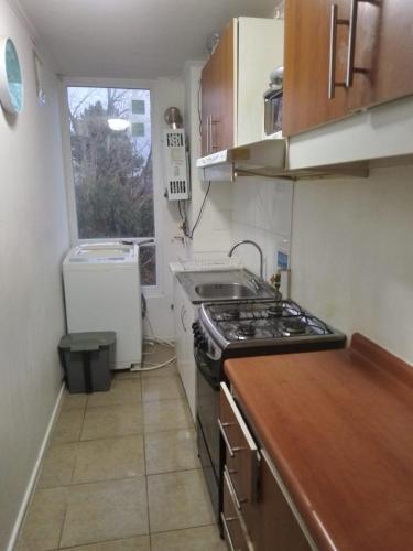 Il comprend une petite cuisine avec une cuisinière et une fenêtre. dans l'établissement Departamento en Condominio, à Puerto Montt