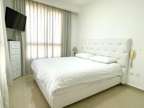 Un dormitorio blanco con una cama grande y un televisor. en LOVELY 2BR GOLF RESIDENCE EILAT, en Eilat