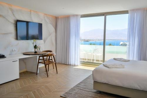 a hotel room with a bed and a desk with a view at AKOYA HOTEL in Eilat