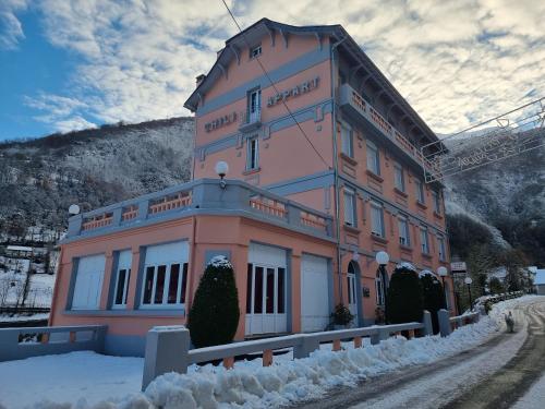 un gran edificio rosa con nieve alrededor en Appart Résidence Le Chili - Lit fait - Parc - Quartier thermal, en Luz-Saint-Sauveur