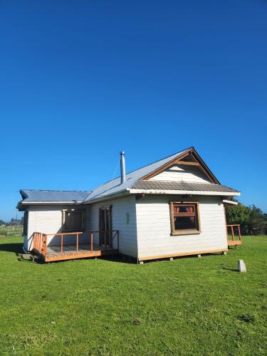 a white house with a porch on a grass field at Cabaña Alto Naupe in Puerto Saavedra
