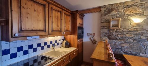 cocina con fregadero y pared de piedra en travelski home premium - Résidence Les Hauts Bois 4 stars, en Aime La Plagne