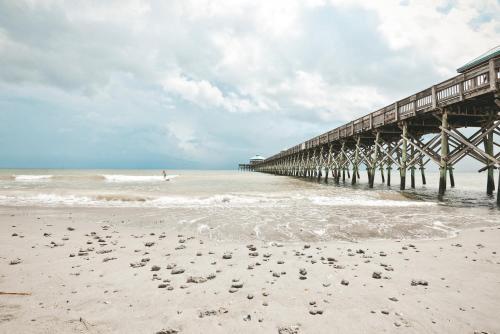 a pier on the beach with a person in the water at The Folly Feeling 1 Block to Beach in Folly Beach