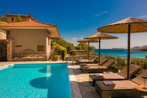 a pool with chairs and umbrellas next to a house at Paramithenio Village Beach Resort & Spa in Áyioi Apóstoloi