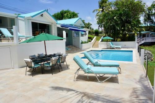 Un patio con mesa y sillas y una piscina. en La Mer - Bright & Modern 3 bedroom Caribbean Villa villa, en Cap Estate