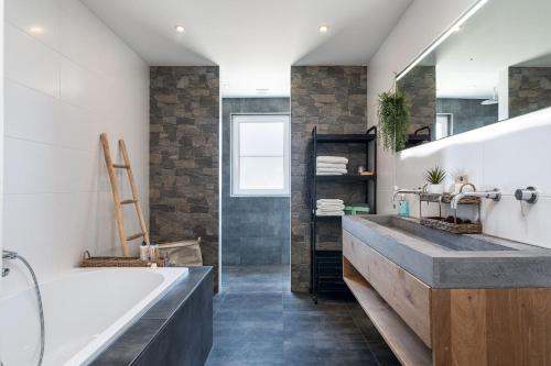 een badkamer met een groot bad en een wastafel bij Luxe bosvilla De Paradijsvogel in Rijs