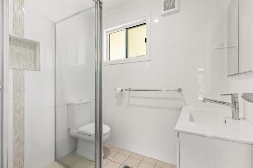 a white bathroom with a toilet and a window at Rocks Place by Experience Jervis Bay in Vincentia