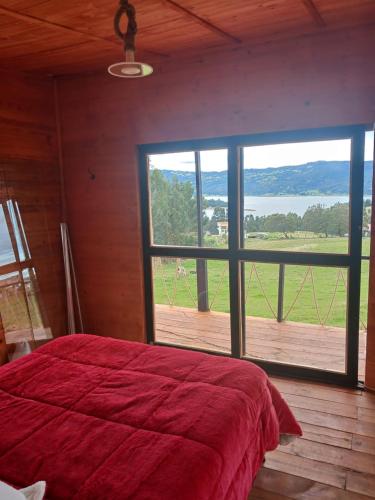 Un dormitorio con una gran cama roja y una gran ventana en Hospedaje cabaña Guatavita Finca las Acacias, en Guatavita