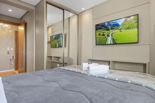 ein Schlafzimmer mit einem großen Bett und einem TV an der Wand in der Unterkunft Jardins de Gramado 402 B - 3 suítes e linda vista in Gramado