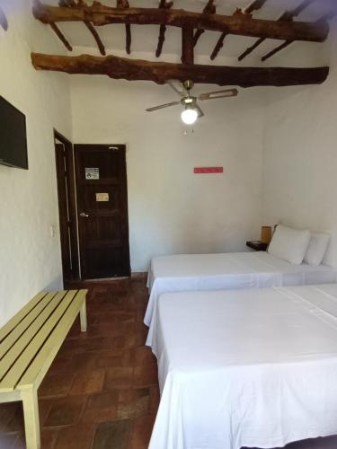 two beds in a room with a bench and a ceiling at Casona CHARA in Barichara