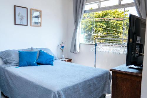 a bedroom with a bed with blue pillows and a window at Otimo studio c WiFi no centro de Pedro Leopoldo MG in Pedro Leopoldo