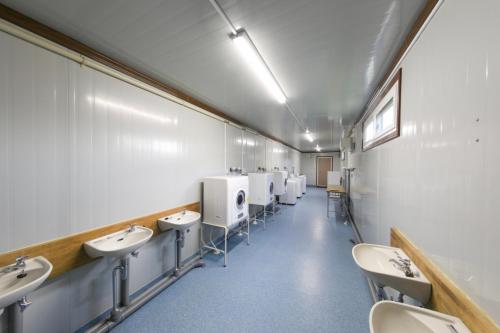 La salle de bains est pourvue d'une rangée de lavabos et de toilettes. dans l'établissement コンテナハウス通天, 