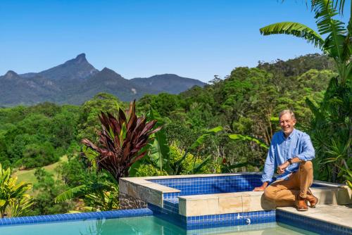 a man sitting next to a swimming pool with mountains in the background at La Rochér Eco Retreat in Stokers Siding