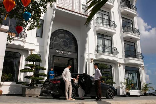 Due uomini in piedi accanto a un'auto di fronte a un edificio. di Serene Nature Hotel & Spa a Hoi An