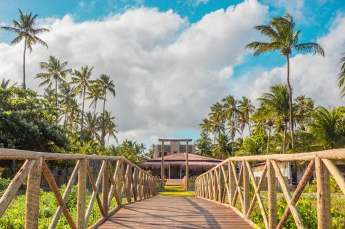 a wooden bridge in front of a resort with palm trees at POUSADA E RESTAURANTE GAROUPA in São Miguel dos Milagres