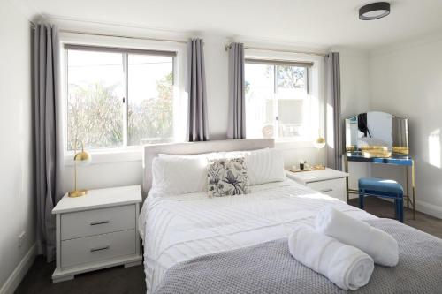 a bedroom with a white bed and two windows at Beach Vibe at Terrigal in Terrigal