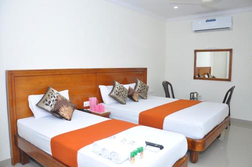 2 letti in una camera d'albergo con arancio e bianco di HOTEL NNP GRAND Rameswaram a Rāmeswaram