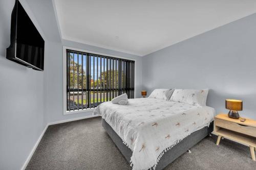 a white bedroom with a large bed and a window at Heather Merimbula in Merimbula