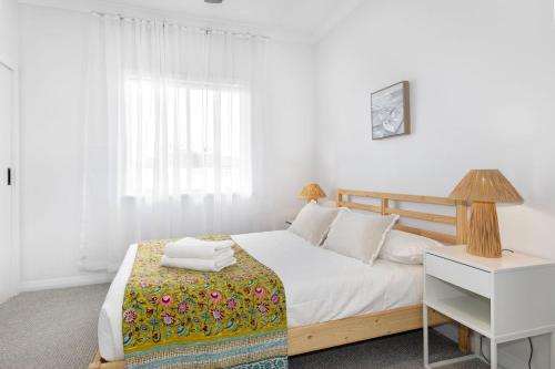 a white bedroom with a bed and a night stand at Fairbairn Family Beach Bungalow in Busselton