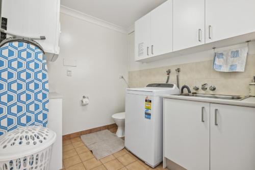 a small white kitchen with a sink and a toilet at Diggers Beach Surf House in Coffs Harbour